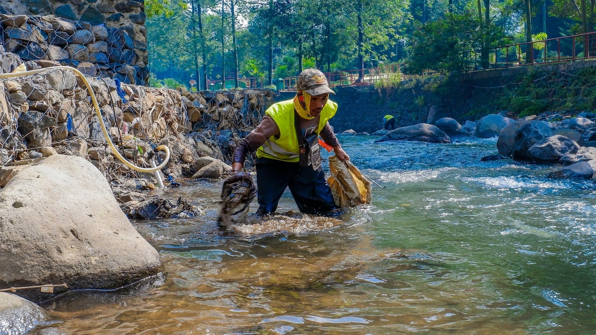 Trabalhador de colete refletivo fazendo a limpeza das margens de um rio