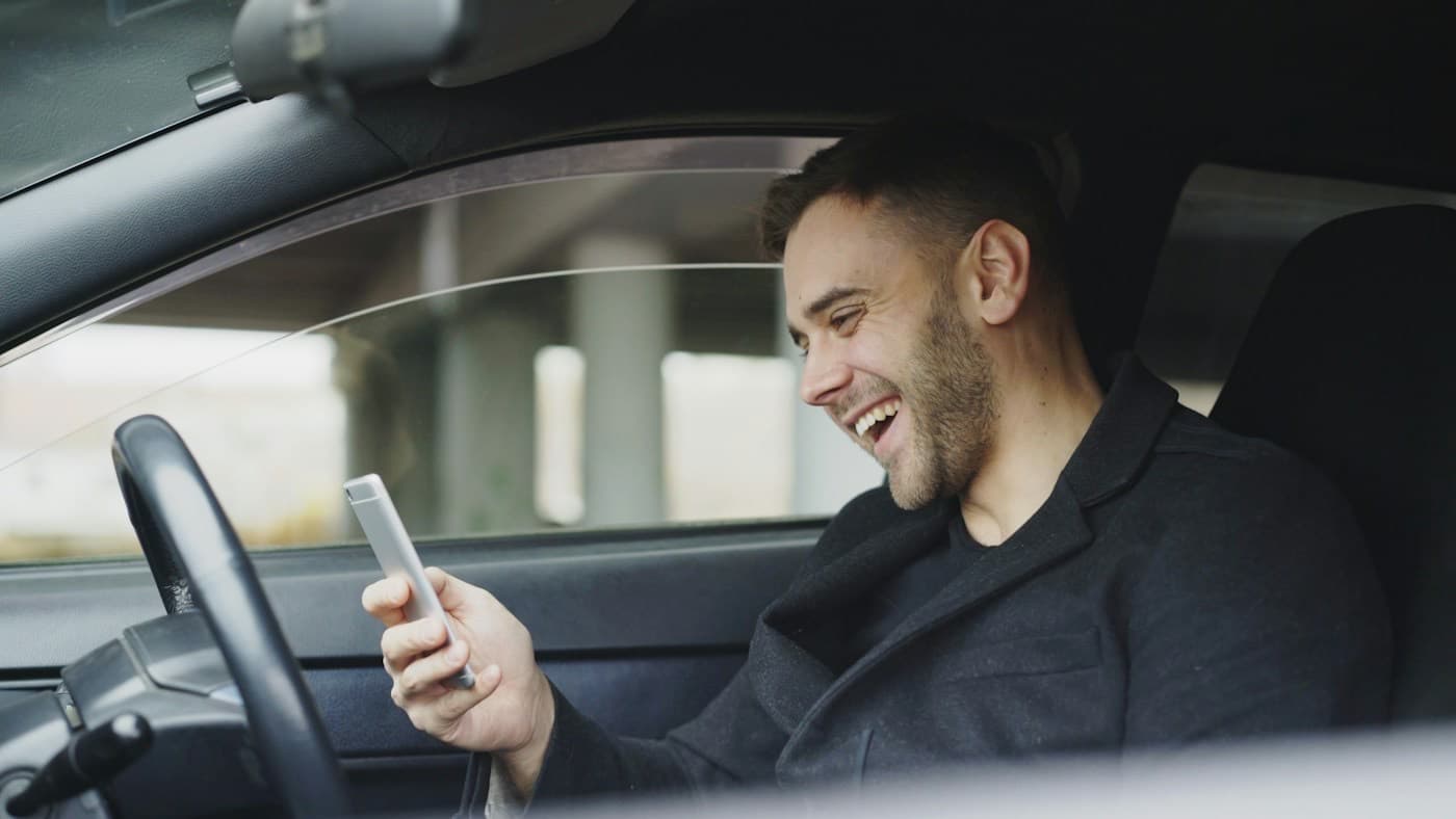 Motorista sorrindo ao conferir o celular dentro do carro