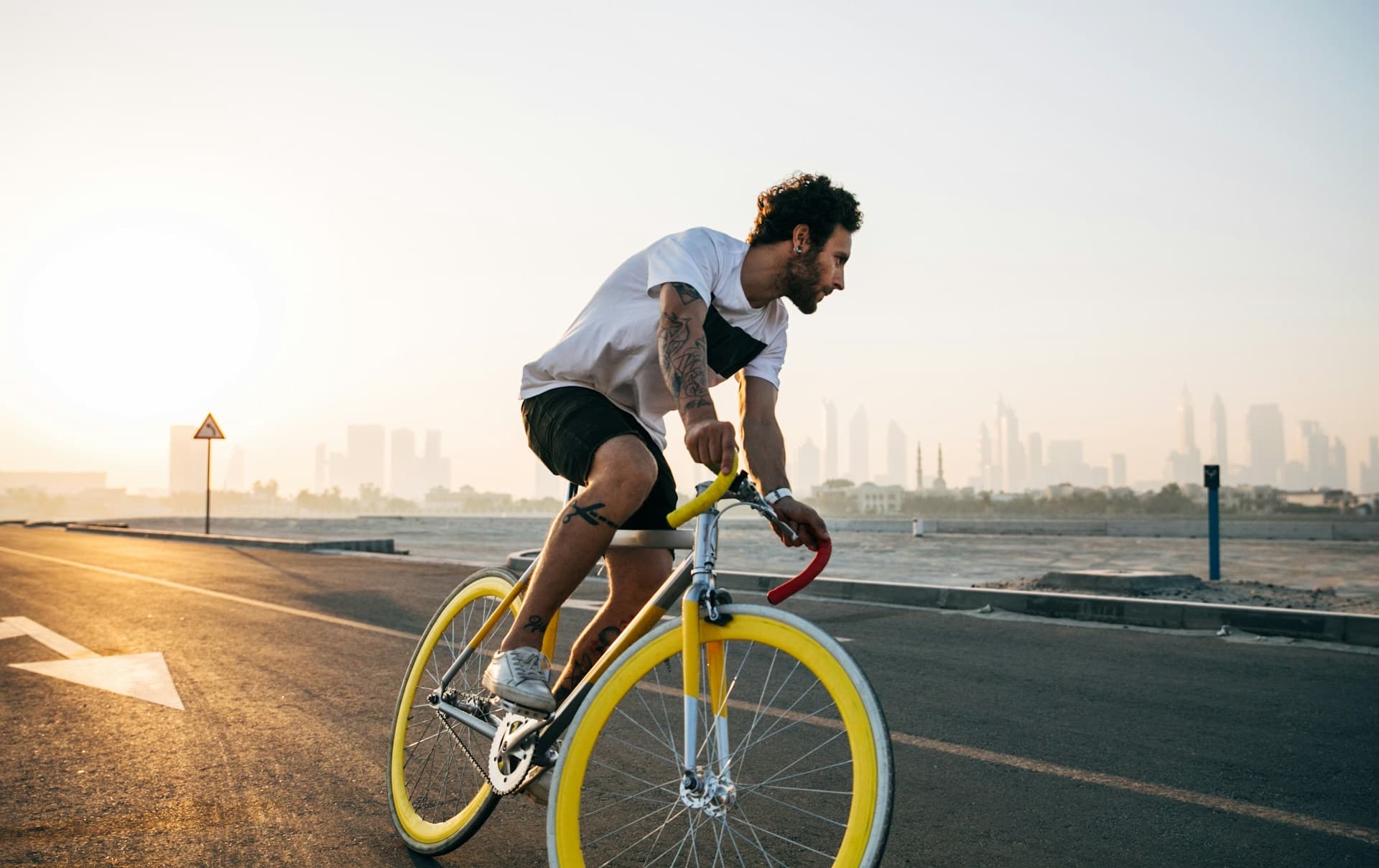 Ciclista pedalando uma bicicleta de estrada na orla ao amanhecer, com a cidade ao fundo