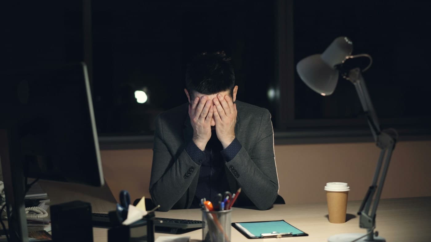 Gestor com as mãos no rosto, sozinho no escritório à noite