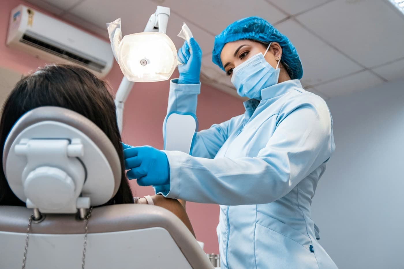 Dentista de máscara e touca atendendo um paciente no consultório