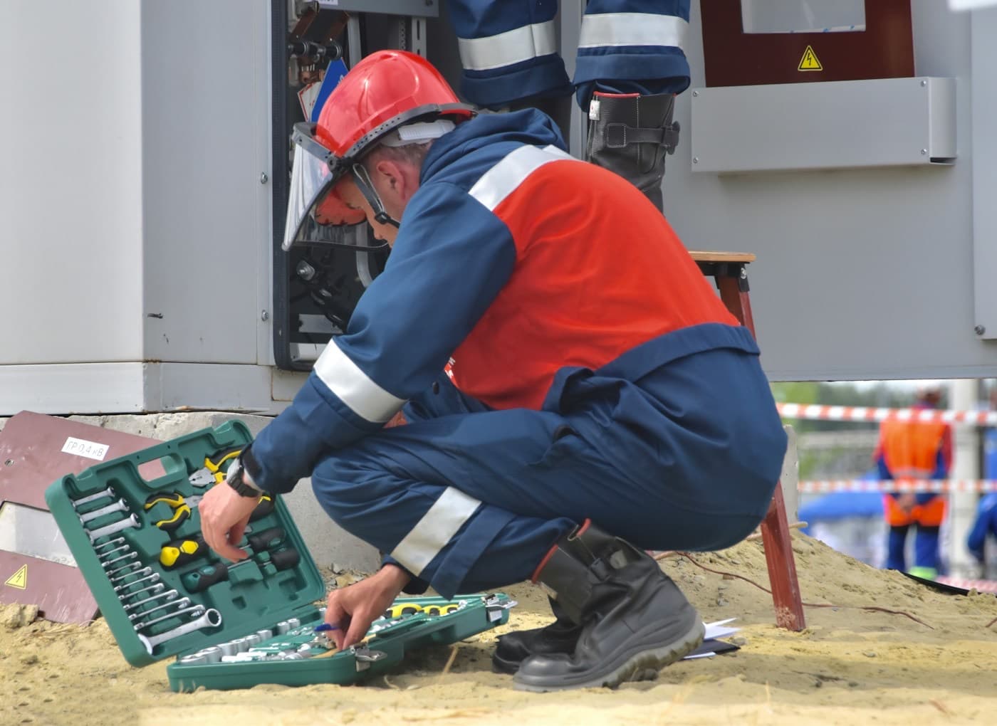 Técnico de capacete agachado ao lado de uma caixa de ferramentas durante uma manutenção