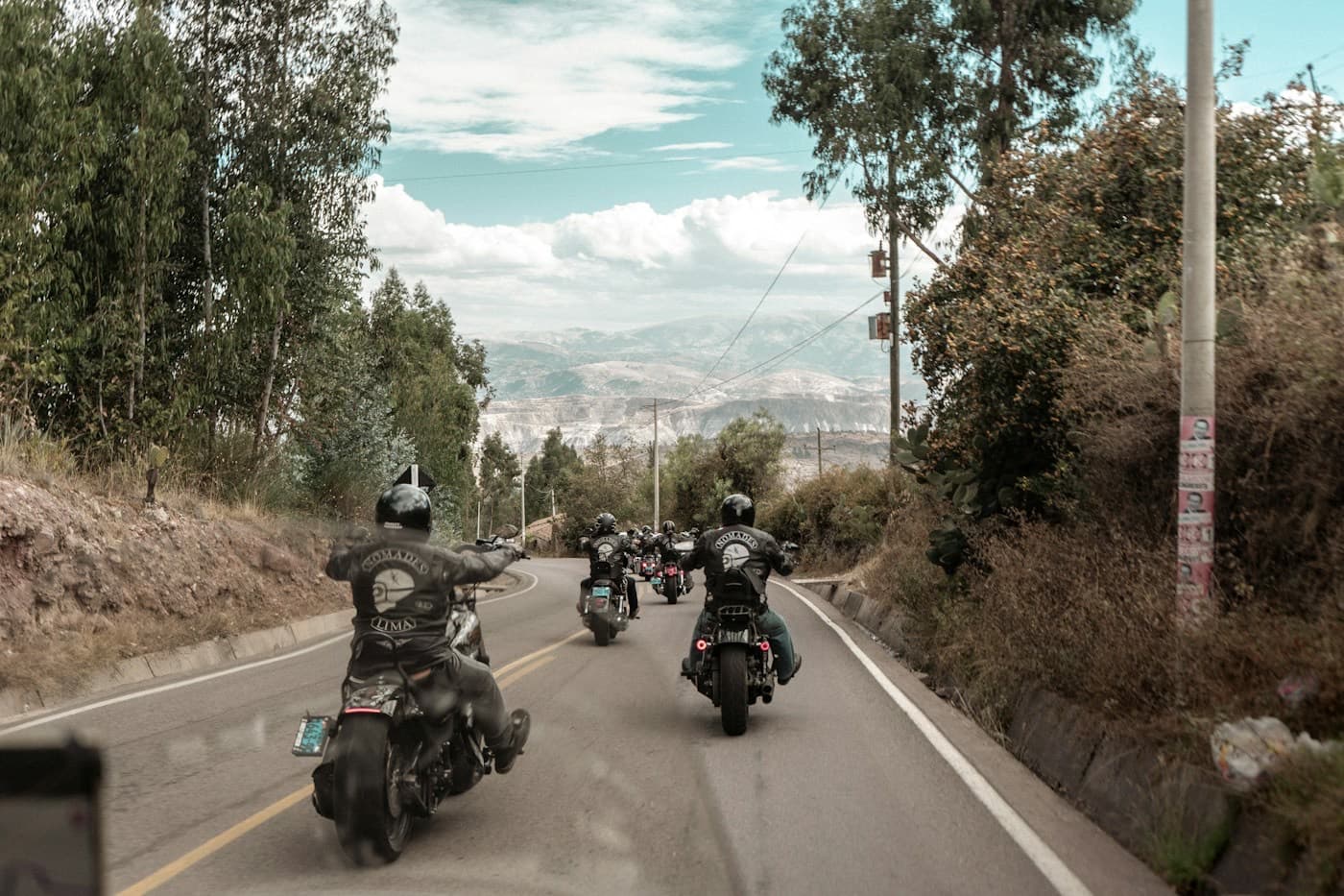 Grupo de motociclistas rodando por uma estrada arborizada