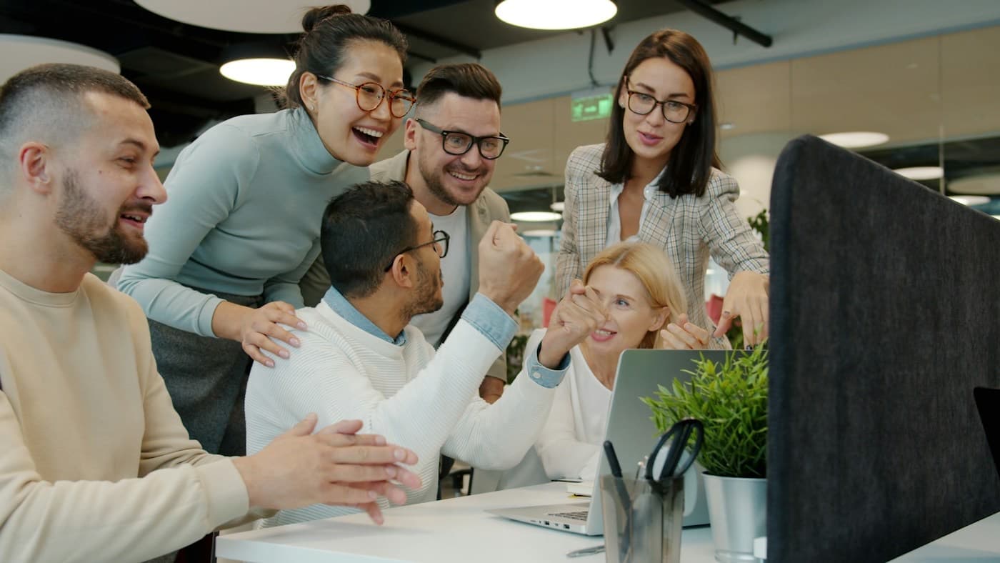 Equipe comemorando reunida em volta de um notebook no escritório