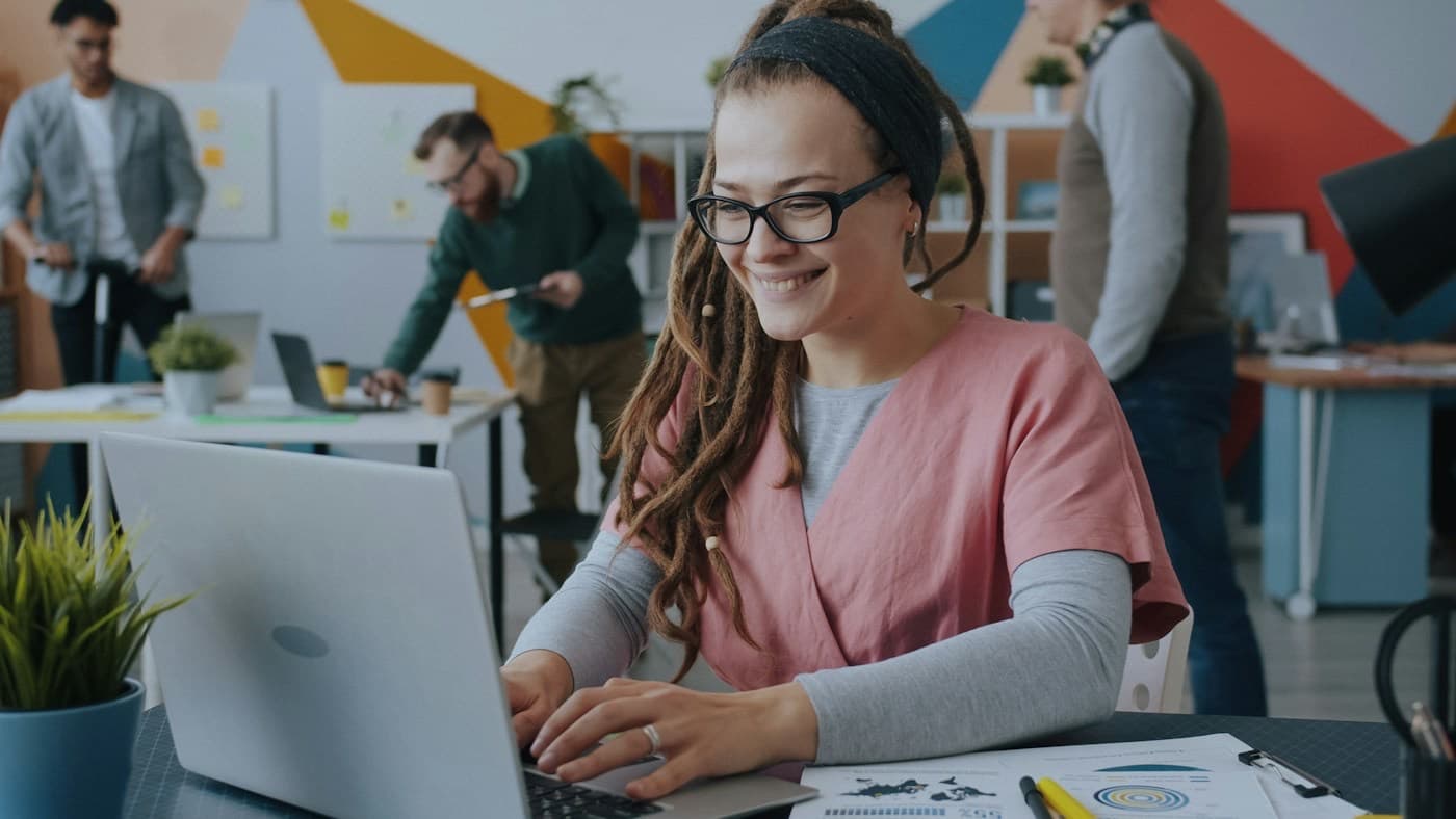 Profissional sorrindo enquanto trabalha no notebook em um escritório