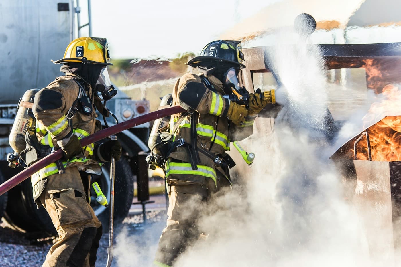 Dois bombeiros combatendo um incêndio com uma mangueira