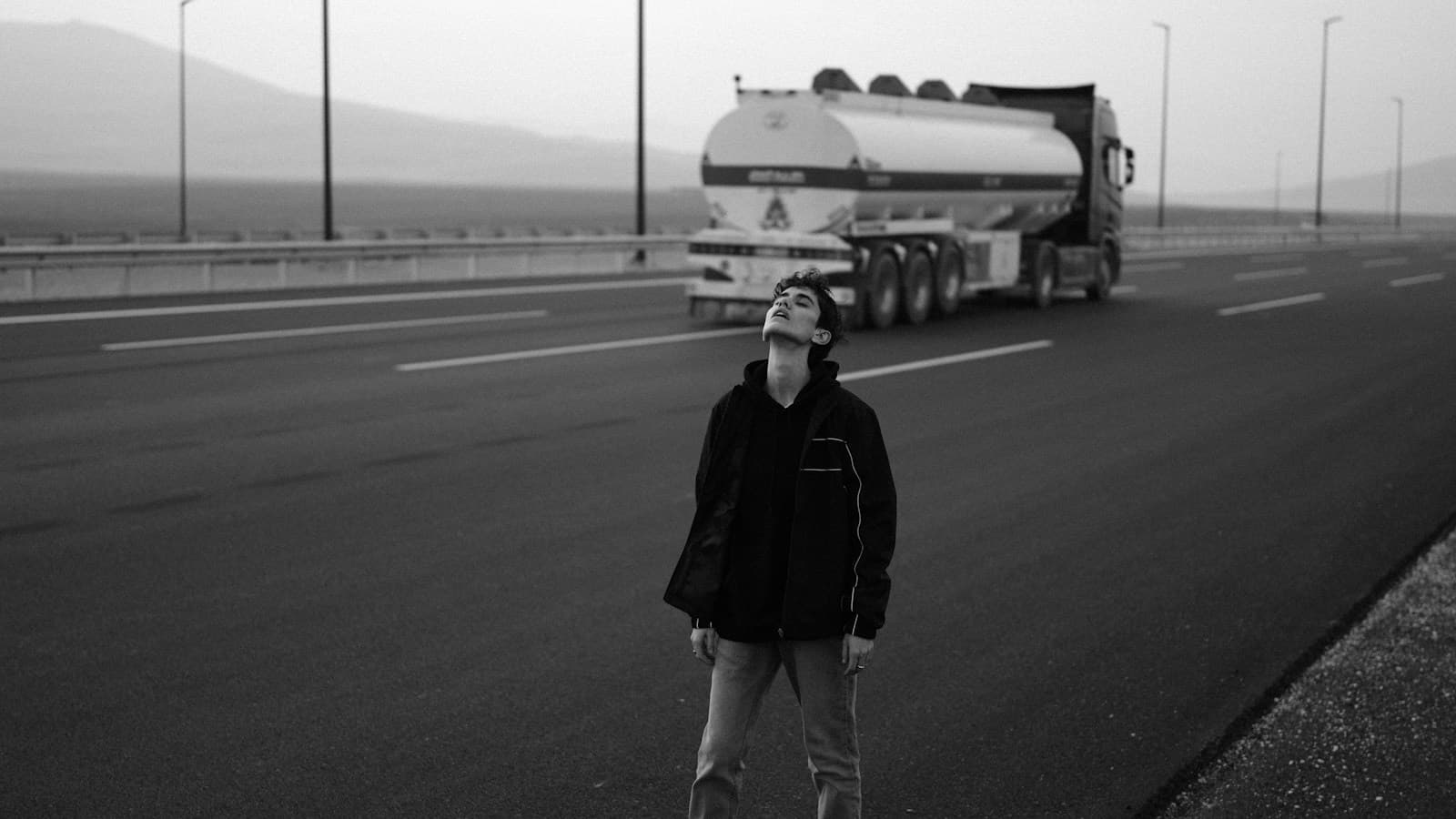 Caminhoneiro em pé na rodovia com um caminhão-tanque ao fundo