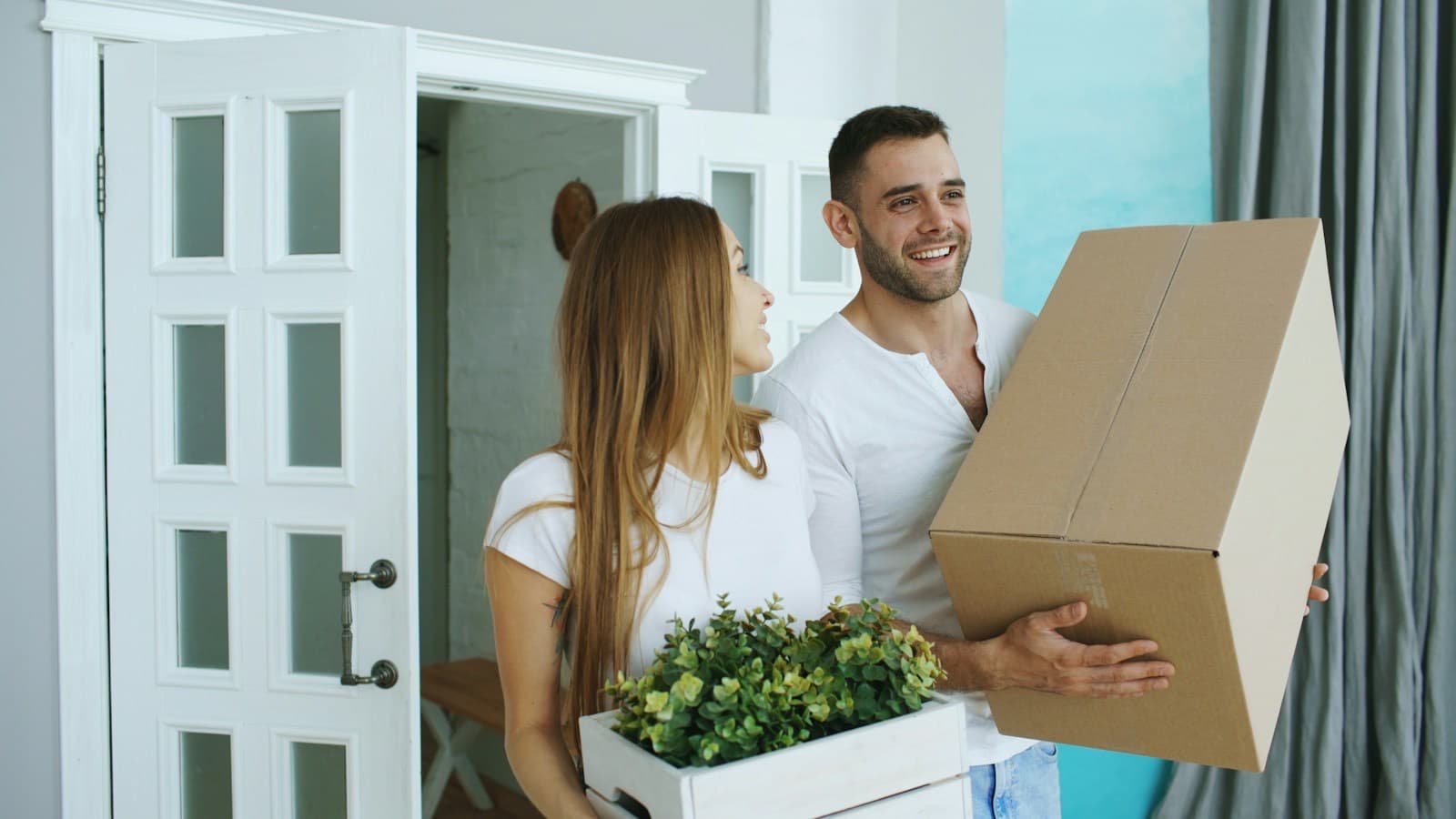 Casal sorrindo ao entrar no novo apartamento com caixas de mudança