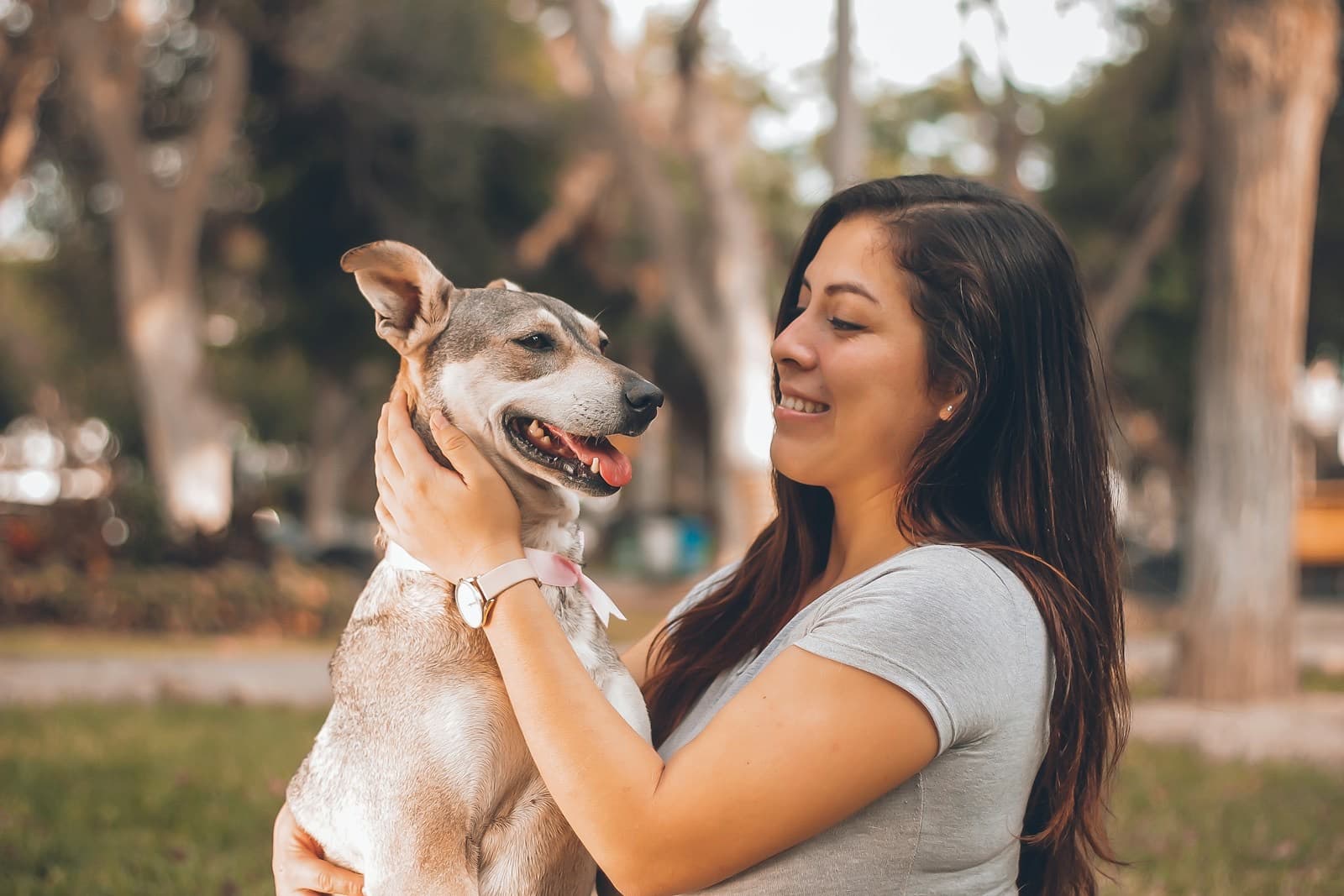 Mulher sorrindo e fazendo carinho em seu cachorro no parque